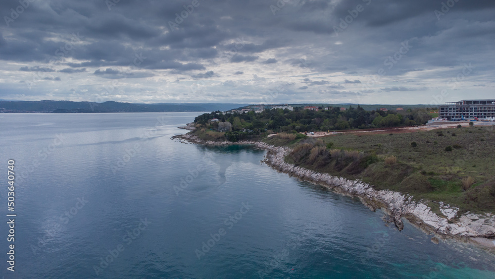 Rocky beach around Savudrija or Alberi area viewed from above. Drone view of visible rocks leading into the blue sea on a cloudy day. Typical istrian rock formations and wild camping behind.
