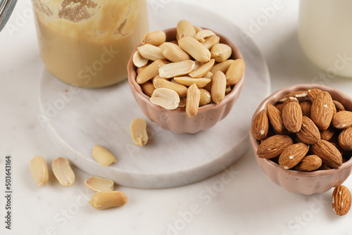 Peanuts, almonds in pink bowls, homemade peanut butter and almond milk on marble boards. Close-up on nuts