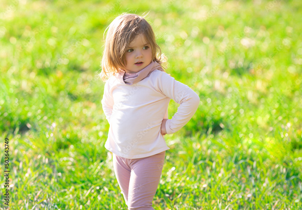 Fototapeta premium Baby girl walking in green grass. Child having fun on family picnic in summer garden.