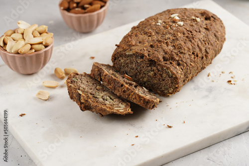 Homemade gluten-free and yeast-free buckwheat whole bread bread loaf with sunflower and pumkin seeds and nuts, cut in slices on white marble board
