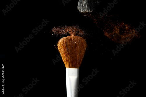 Blusher brush with powder particles on black background photo