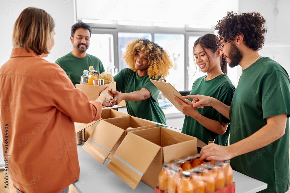 © Syda Productions - charity, donation and volunteering concept - happy smiling male volunteer with clipboard and woman taking box of food at distribution or refugee assistance center