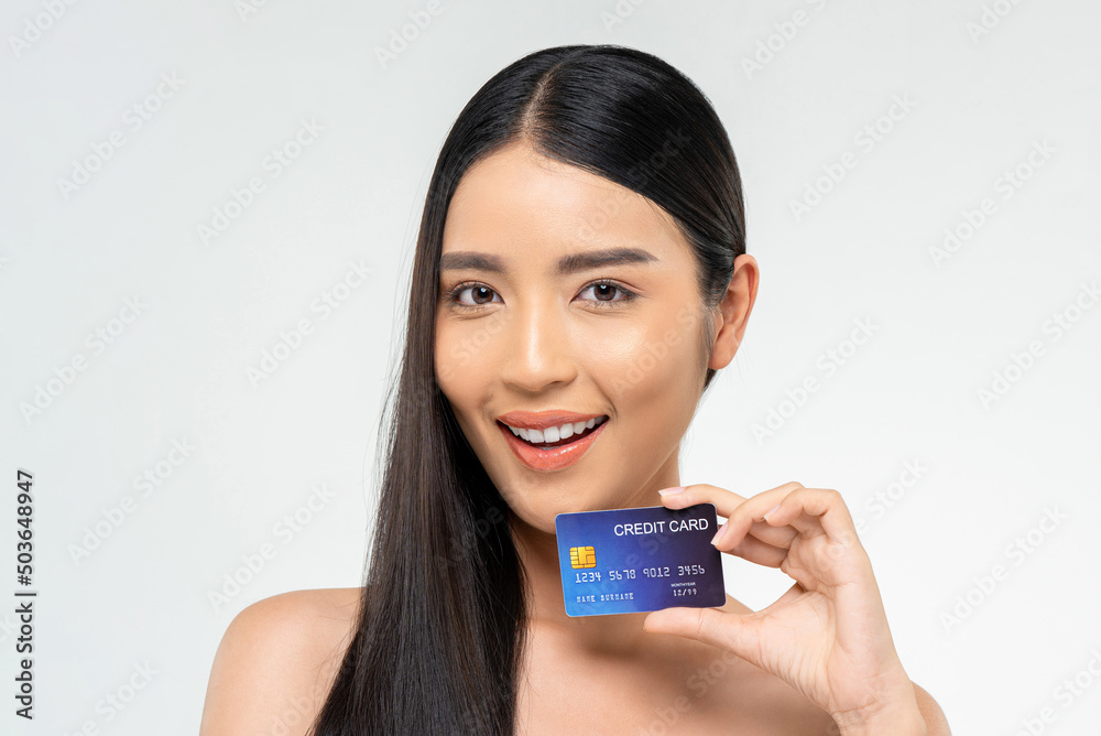 Beauty shot of cheerful Asian female with long dark hair showing credit card on white isolated background in studio
