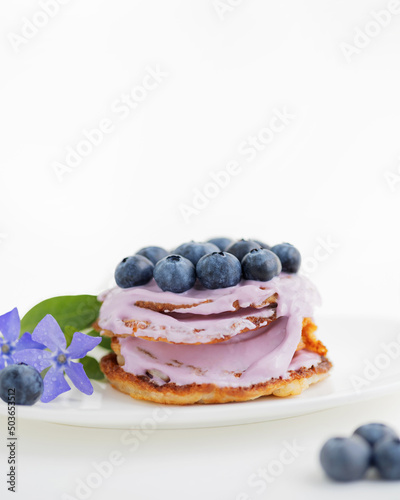 Pancakes with blueberries and yogurt on a white plate with violets flowers. White background with copy space 