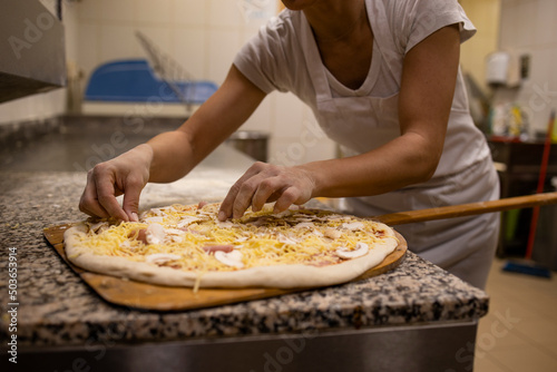 Close up view of baker preparing pizza dough and topping for baking.