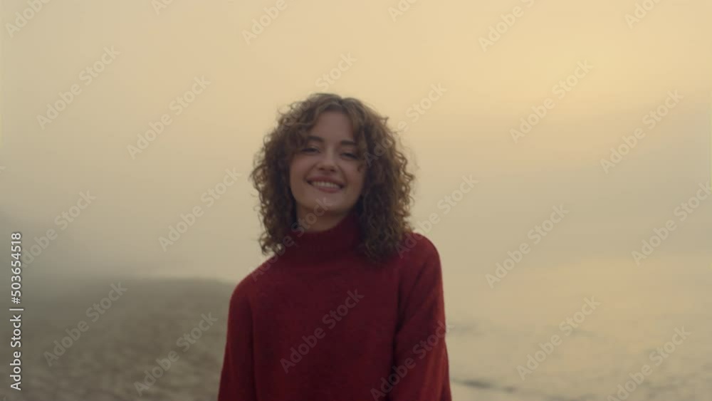 Smiling girl posing at camera. Happy woman posing on sea beach at sunrise Smiling girl posing at camera. Happy woman posing on sea beach at sunrise