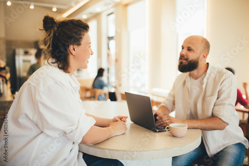 Young man and woman discussing project using laptop, sitting in a coffee house.