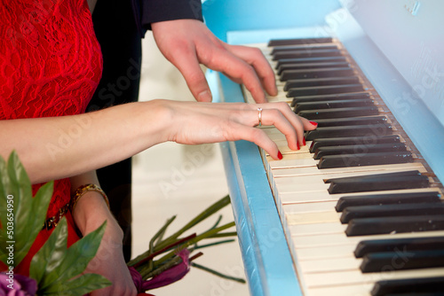 Woman's hand with a wedding ring on the piano. In the background is a man. © Veronika Klim