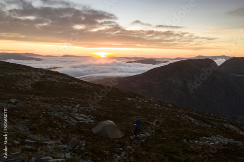 A man and wild camping tent on a mountain at sunset
