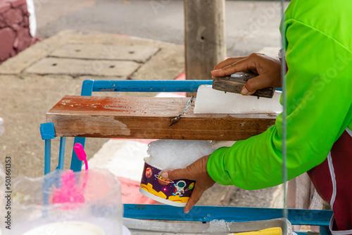 
The seller is scraping ice cubes with a blade on the wood to obtain ice crystals. Used to make desserts, shaved ice Thailand