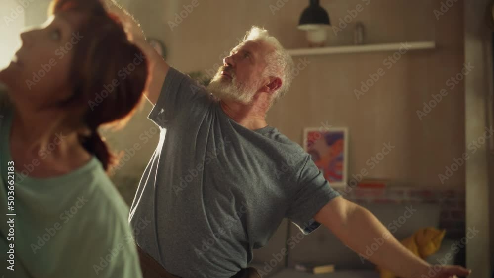 Close Up Portrait of a Senior Couple Doing Gymnastics and Yoga Stretching Exercises Together at Home on Sunny Morning. Concept of Healthy Lifestyle, Fitness, Recreation, Couple Goals and Retirement. Close Up Portrait of a Senior Couple Doing Gymnastics and Yoga Stretching Exercises Together at Home on Sunny Morning. Concept of Healthy Lifestyle, Fitness, Recreation, Couple Goals and Retirement.