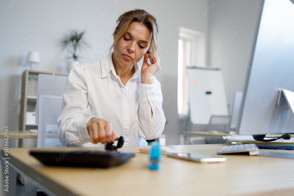© Andrii  - Female office worker putting on wireless headphones