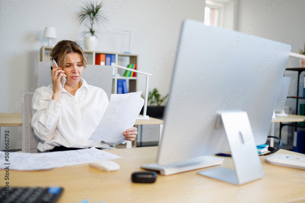 Woman accountant indignantly looks at documents and talks on the smartphone Woman accountant indignantly looks at documents and talks on the smartphone