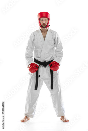 Portrait of young sportive man wearing white dobok, helmet and gloves posing isolated over white background. Concept of sport, workout, health.