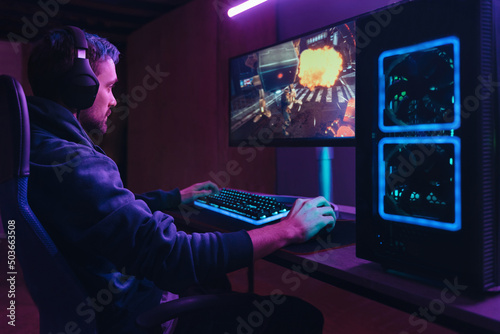 Obraz na płótnie Young concentrated cyber sportsman playing in FPS video game on his personal computer in dark neon room