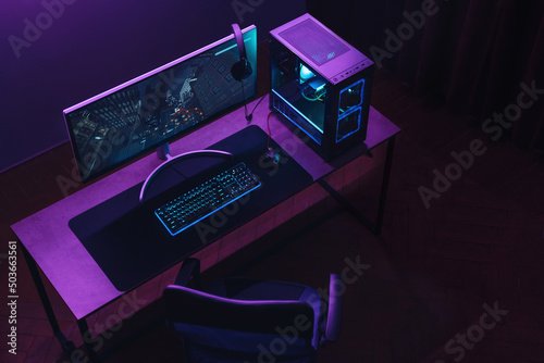 Top view of gamer work space and professional gaming setup: mouse, keyboard, monitor, headset, powerful computer. Premium PC with RGB light inside. Cyber sportsman empty studio with streaming setup