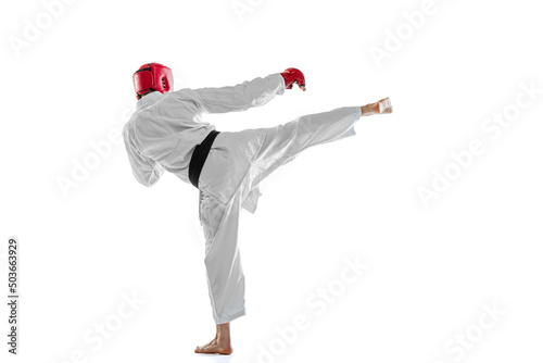 Back view. Portrait of young sportive man wearing white dobok, helmet and gloves practicing isolated over white background. Concept of sport, workout, health.