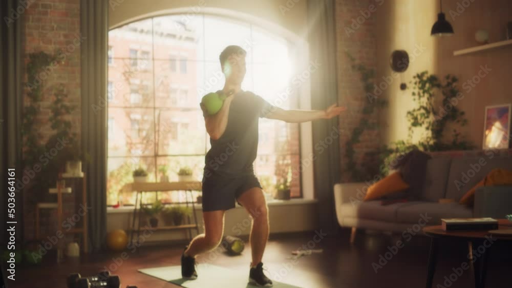 Strong Athletic Fit Young Man Lifting a Heavy Kettlebell, Doing Core Strengthening Exercises During Morning Workout at Home in Sunny Apartment. Concept of Health and Fitness. Strong Athletic Fit Young Man Lifting a Heavy Kettlebell, Doing Core Strengthening Exercises During Morning Workout at Home in Sunny Apartment. Concept of Health and Fitness.