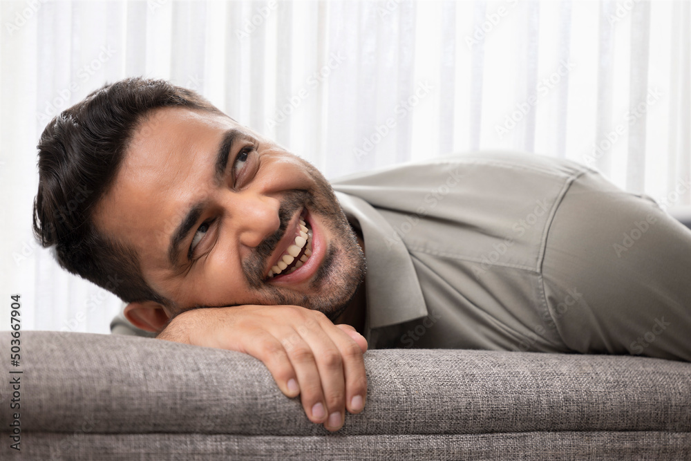 Close-up portrait of a cheerful young man leaning head on sofa and looking above Close-up portrait of a cheerful young man leaning head on sofa and looking above