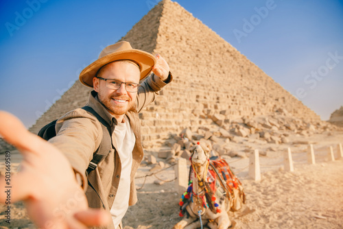 Selfie photo man in hat background pyramid of Egyptian Giza and camel, sunset Cairo, Egypt