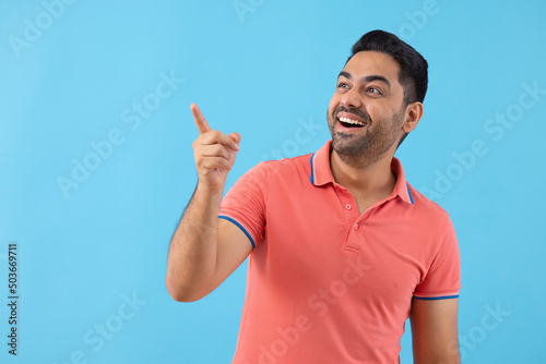 Smiling young man pointing elsewhere against blue background