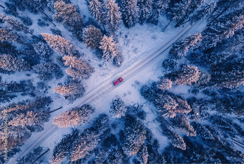 Red car driving on winding road through snowy forest, toning blue. Concept winter travel, aerial view