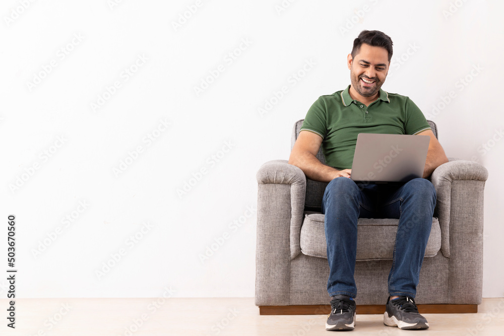 Portrait of a cheerful young man using laptop while sitting on sofa Portrait of a cheerful young man using laptop while sitting on sofa