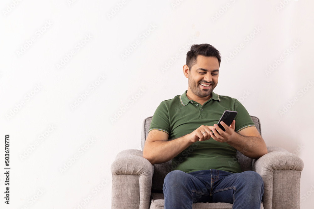 Cheerful young man using Smartphone while sitting on sofa