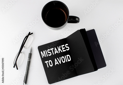 MISTAKES TO AVOID written text in small black notebook with coffee , pen and glasess on white background. Black-white style