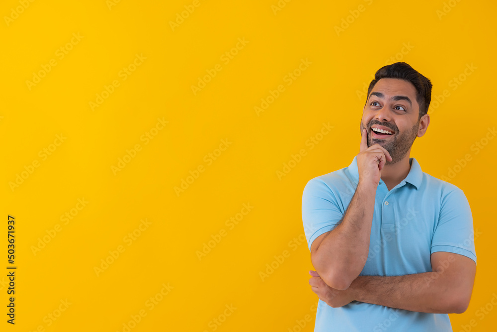 Portrait of a cheerful young man looking elsewhere with hand on cheek against yellow background Portrait of a cheerful young man looking elsewhere with hand on cheek against yellow background