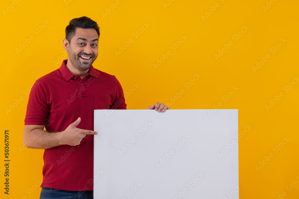 Portrait of a cheerful young man on yellow background pointing at blank placard Portrait of a cheerful young man on yellow background pointing at blank placard