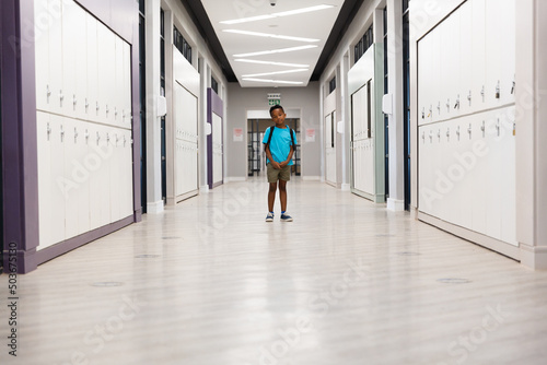 Full length of african american elementary schoolboy standing amidst lockers in corridor
