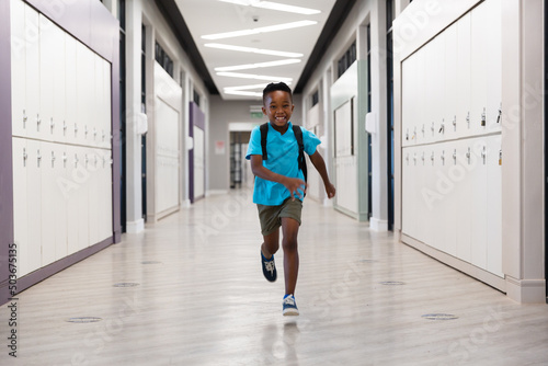 Full length of smiling african american elementary schoolboy running in corridor at school