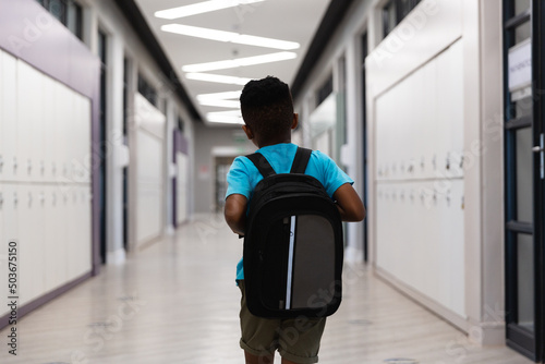 Rear view of african american elementary schoolboy with backpack walking in school corridor