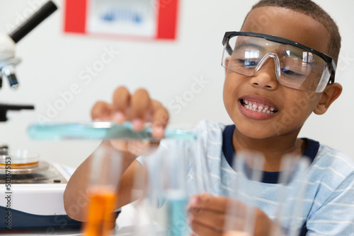 Smiling african american elementary schoolboy performing chemistry practical in laboratory