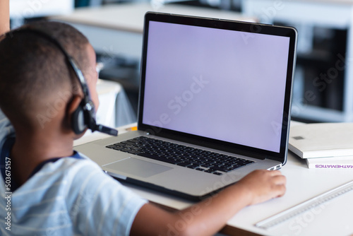 African american elementary schoolboy wearing headphones while using laptop with copy space