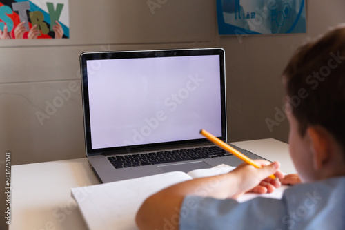 Caucasian elementary schoolboy using laptop while studying at desk in school