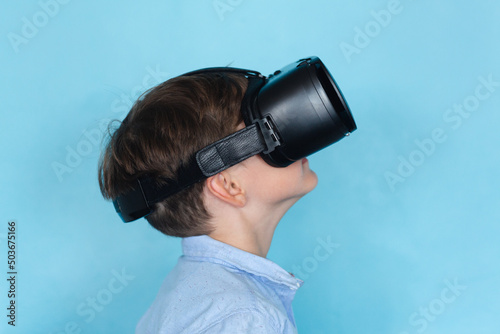 Side view of caucasian elementary schoolboy wearing vr glasses against blue background