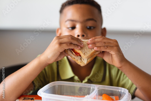 Close-up of african american elementary schoolboy eating sandwich during lunch break in class