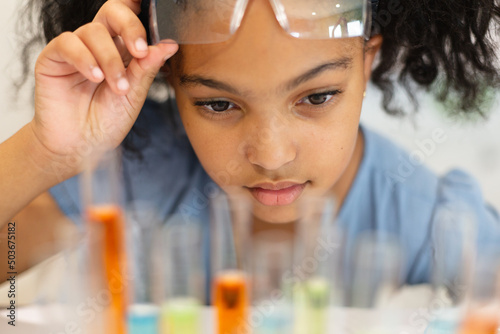 Close-up of biracial elementary schoolgirl looking at chemicals in test tubes during chemistry class
