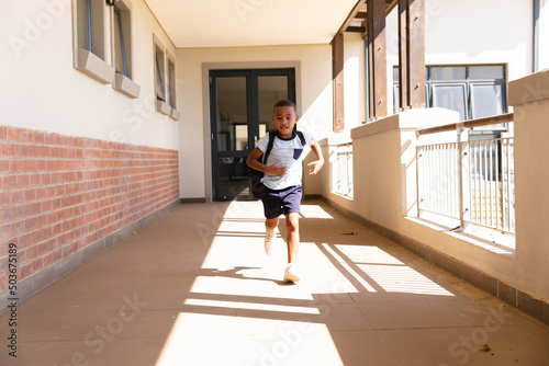 Full length of african american elementary schoolboy with backpack running in school corridor