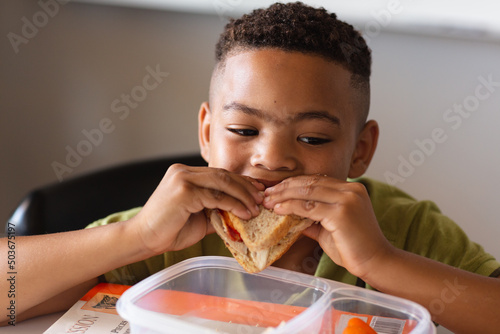 Close-up of african american elementary schoolboy eating sandwich at desk during lunch break