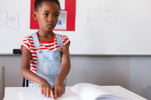 Blind african american elementary schoolgirl touching braille book while studying in classroom