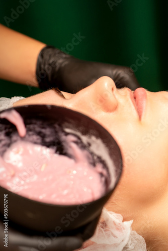 Beautiful young caucasian woman receiving an alginic mask to the face in beauty salon. Facial skin treatment photo