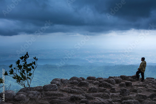 A man stands on the edge of a cliff on a rainy day.