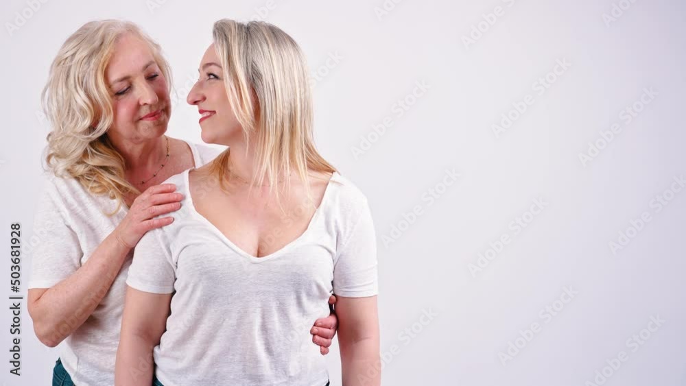 Support concept. Studio shot on white background of two european women in their 40s. One woman standing in the back, putting one hand on her companions shoulder and the other on her friends waist Support concept. Studio shot on white background of two european women in their 40s. One woman standing in the back, putting one hand on her companions shoulder and the other on her friends waist
