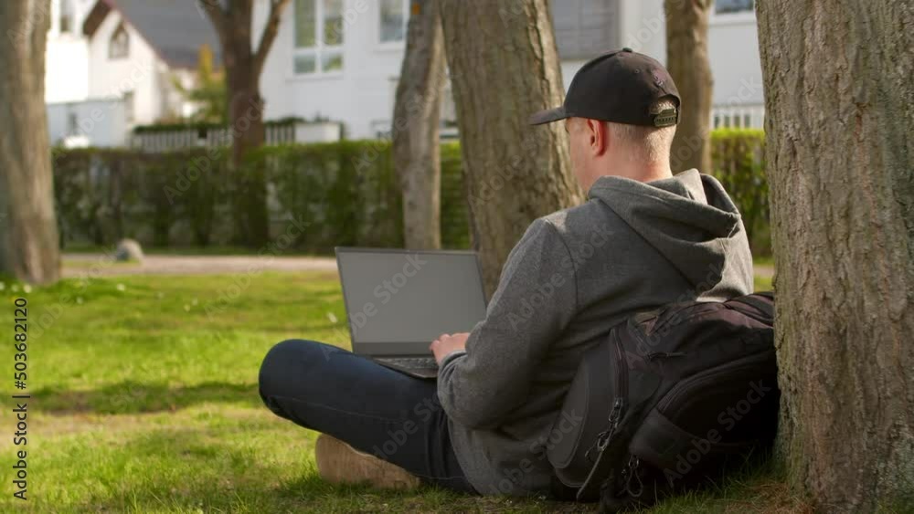 Young man is sitting in a park in a tourist place, working on a laptop. Young man is sitting in a park in a tourist place, working on a laptop.