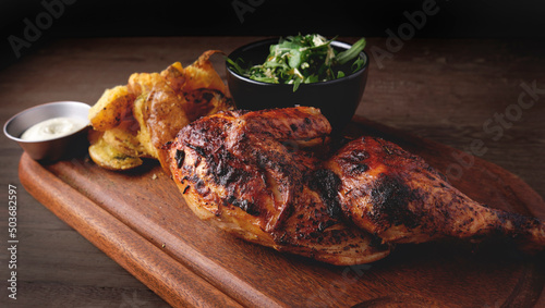 Peruvian food, Pollo a la brasa or grilled half chicken with fried yellow potatoes and arugula salad, wooden board. Selective focus photo