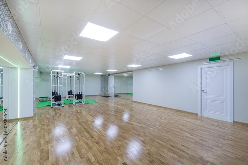 A large  bright gym with brown laminate flooring  an entrance door and sports equipment.