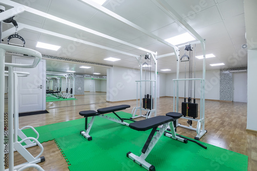 A bright gym room with large mirrors and exercise equipment on green mats.